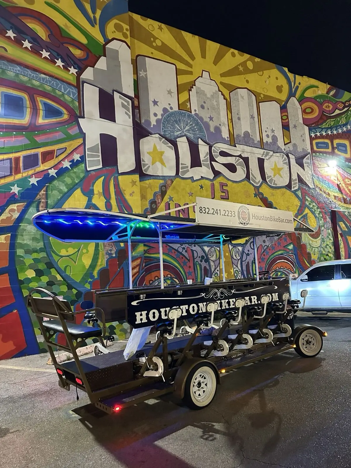 The Houston Bike Bar lit up at night in front of a Houston mural
