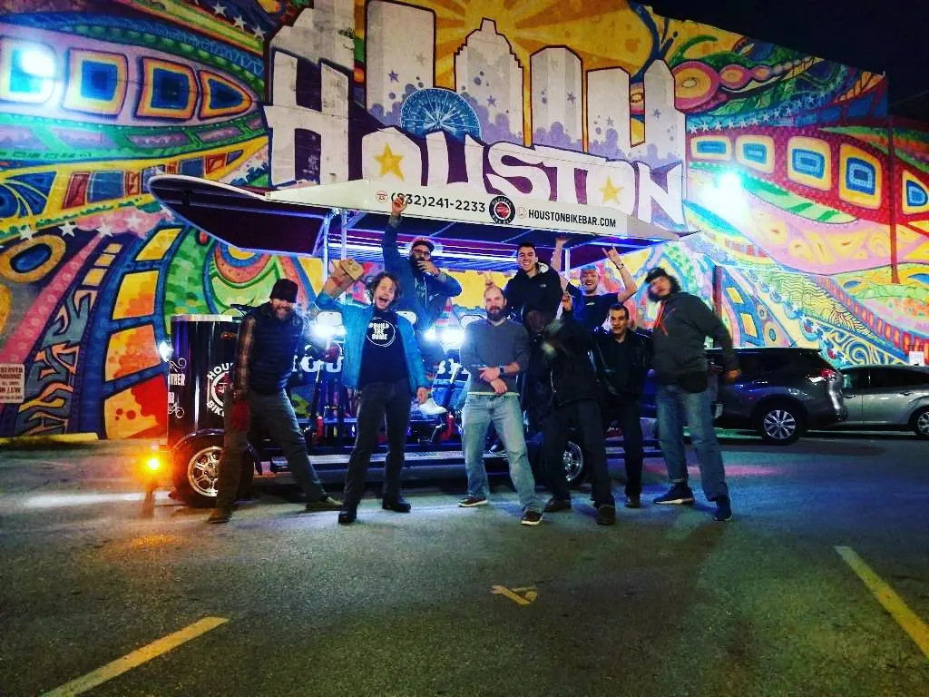 A group posing with the bike bar in front of the Houston mural at night